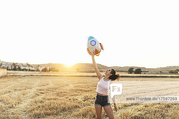 Woman holding aloft artificial rocket balloon at sunset