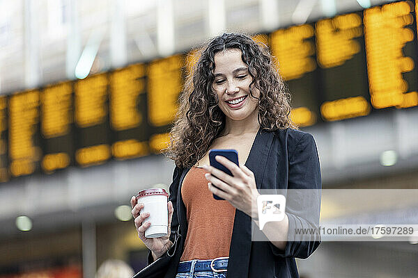 Smiling woman using phone and having coffee