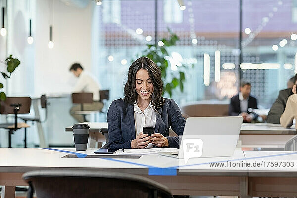 Smiling employee text messaging on mobile phone in office
