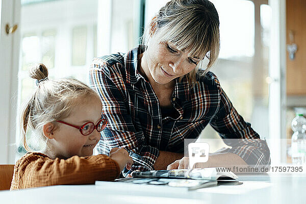Cute girl and mother reading book on table at home