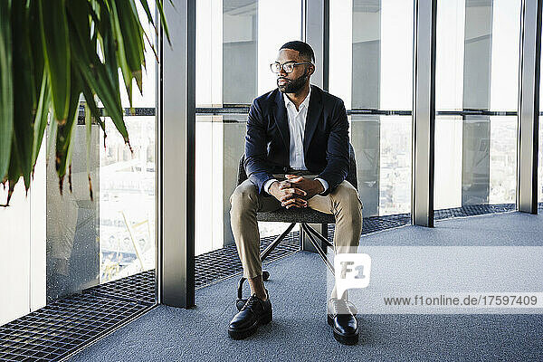 Young businessman with hands clasped sitting on chair in office