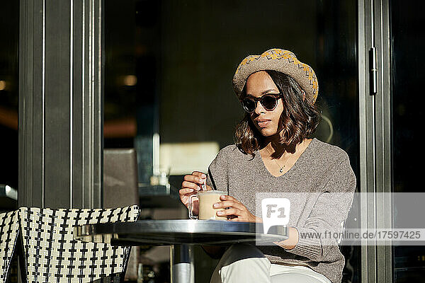 Young woman stirring coffee in cafe on sunny day