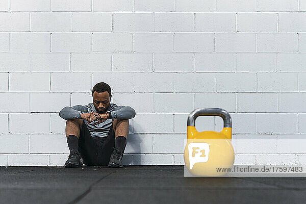 Yellow kettlebell on gym floor with tired athlete sitting in background