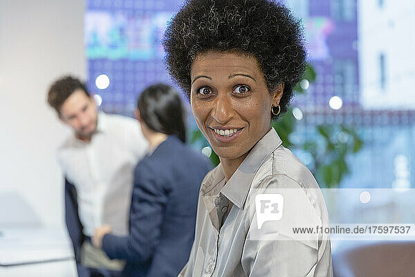 Smiling businesswoman with colleagues in background at coworking space
