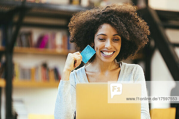 Fröhliche Geschäftsfrau mit Kreditkarte und Laptop im Büro
