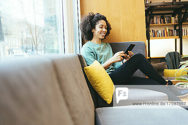 Lächelnde Geschäftsfrau benutzt Smartphone auf dem Sofa