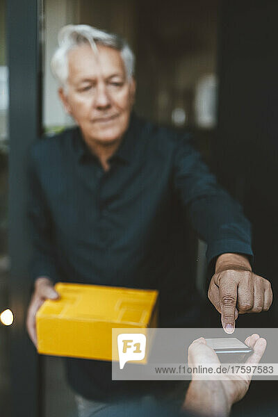 Senior man signing on smart phone held by delivery person