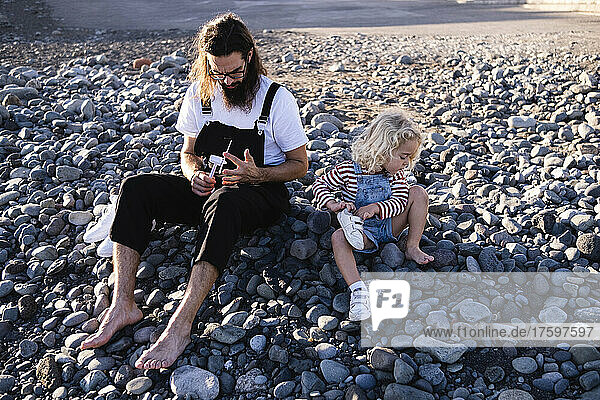 Father and son sitting together on pebbles at beach