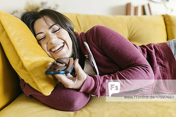 Cheerful woman talking on smart phone through speaker at home