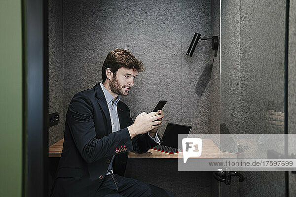 Businessman using smart phone sitting at desk in cabin