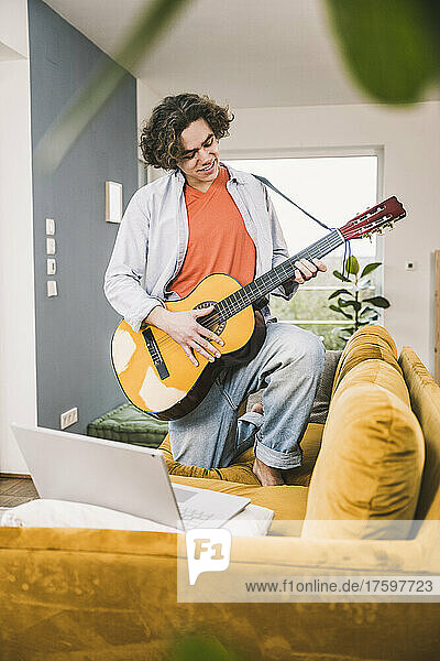 Young man playing guitar on sofa in living room at home