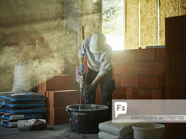 Bricklayer mixing cement in tub at construction site