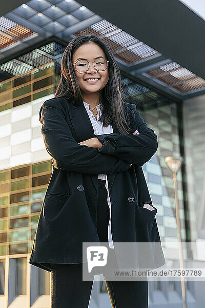 Confident businesswoman with arms crossed standing in front of office building