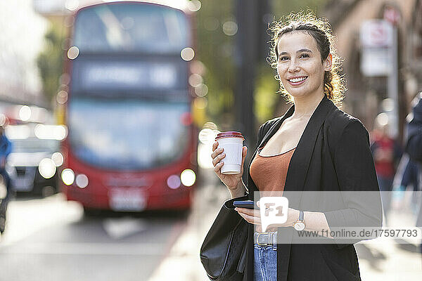 Smiling businesswoman with disposable coffee cup on road in city