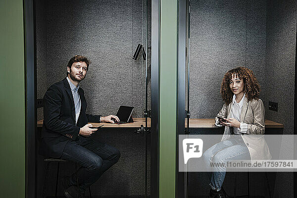 Businesswoman and businessman with mobile phones sitting at desk in cabin