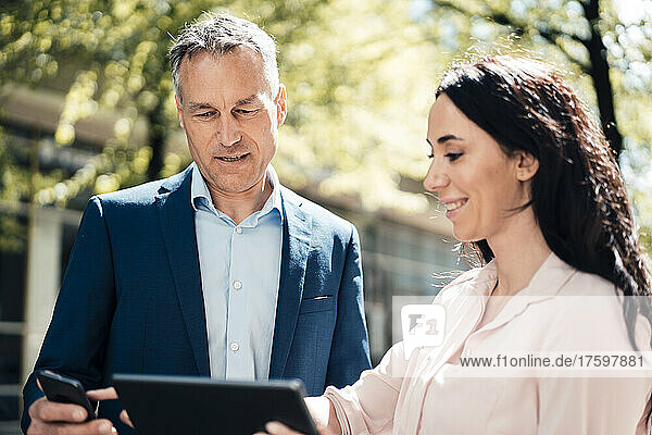 Businesswoman and businessman discussing over wireless technologies on sunny day