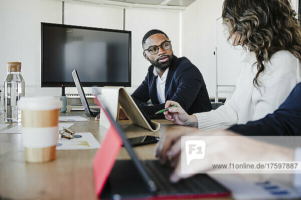 Young businessman wearing eyeglasses discussing strategy with colleague in office