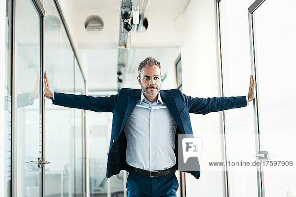 Businessman with arms outstretched in office corridor