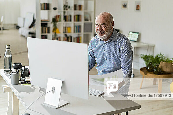 Happy freelancer with document working on computer at home office