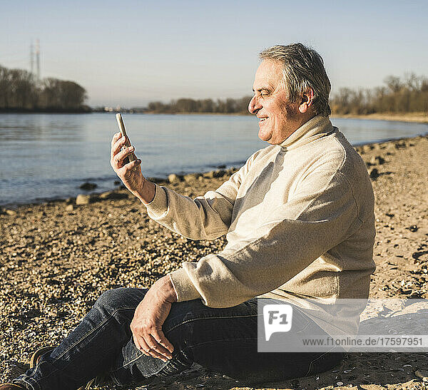 Happy senior man doing video call through mobile phone at beach on sunny day