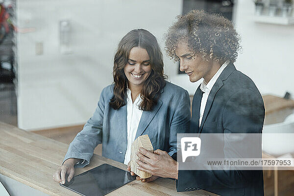 Smiling businessman with tablet PC standing by colleague explaining model house in office