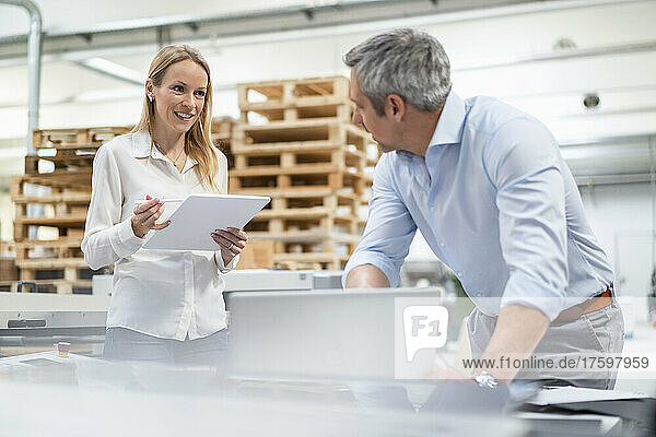 Smiling blond businesswoman holding tablet PC sharing ideas with businessman in industry