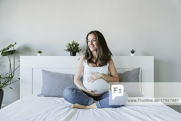Smiling pregnant woman sitting cross-legged on bed at home