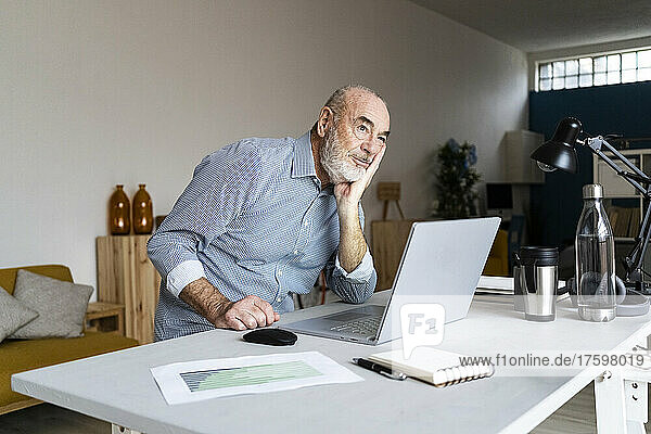 Thoughtful businessman sitting with hand on chin at desk