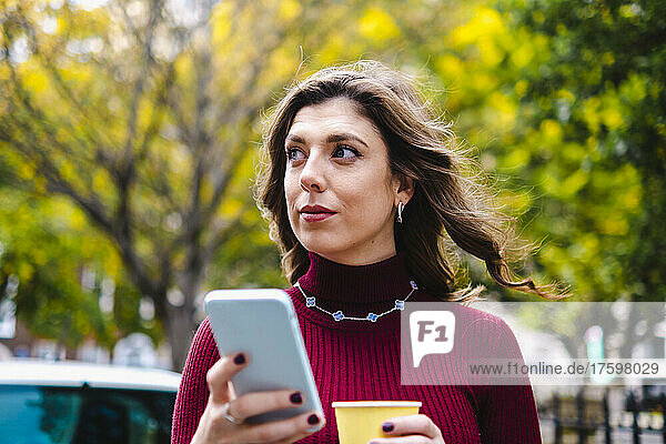 Thoughtful woman with smart phone and coffee cup