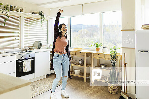 Carefree woman dancing listening music in kitchen at home