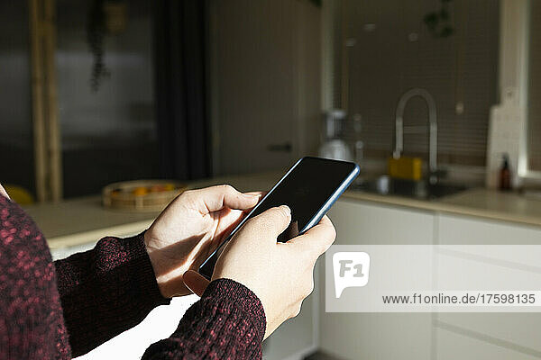 Woman using smart phone in kitchen on sunny day