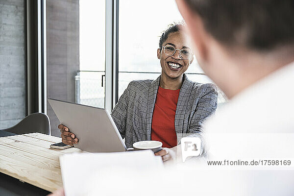 Glückliche Geschäftsfrau  die am Laptop mit einem Kollegen im Büro diskutiert