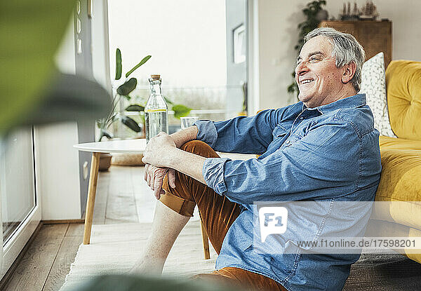 Happy senior man sitting by sofa in living room