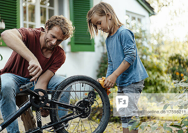 Father helping son repairing bicycle in backyard