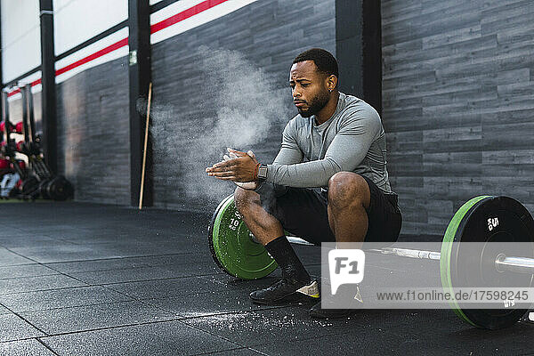 Athlete dusting chalk powder sitting on barbell in gym