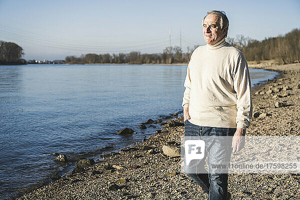 Smiling senior man with hand in pocket walking at beach
