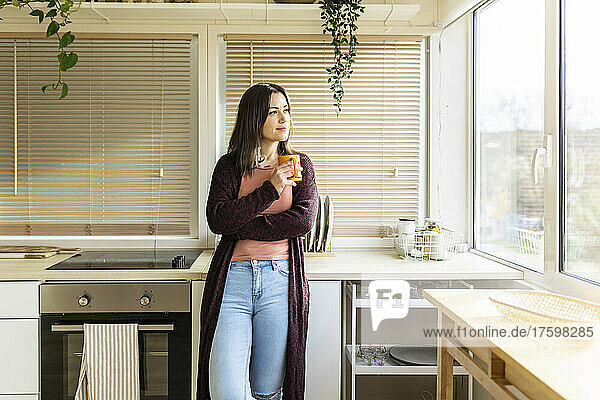 Woman with mug leaning on kitchen counter at home