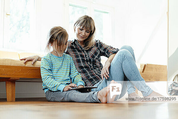 Mother looking at son using digital tablet on floor at home