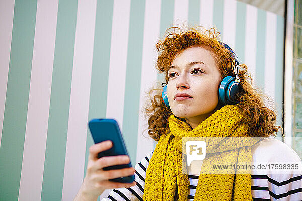 Contemplative woman listening music through headphones in cafe