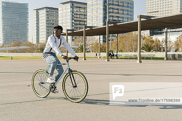 Young man with cap cycling on sunny day in city