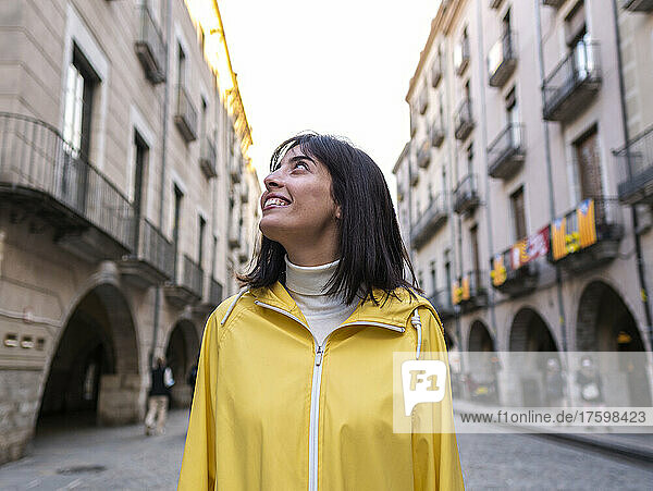 Smiling woman in yellow raincoat standing on footpath in city