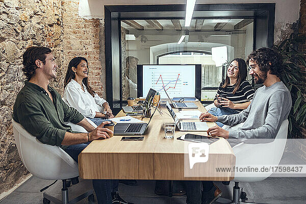 Lächelnde Geschäftsleute und Geschäftsfrauen sitzen am Konferenztisch im Coworking-Büro