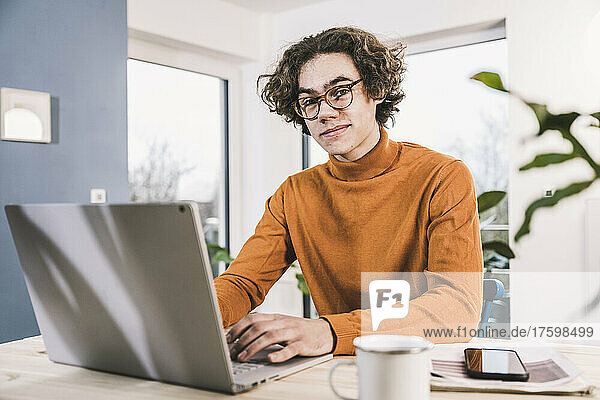 Young man with laptop sitting at table in living room