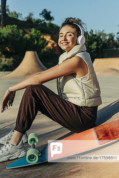 Smiling woman listening music on headphones by skateboard in park