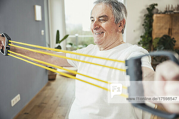 Smiling senior man doing stretching exercise with resistance band at home
