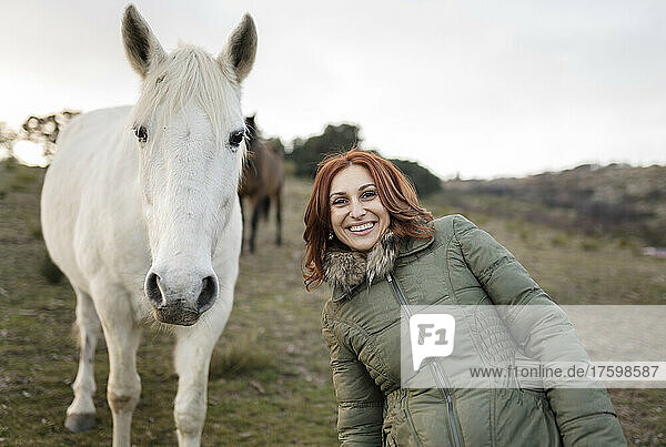 Happy woman standing by white horse in ranch