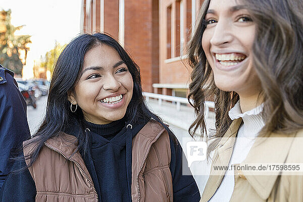 Cheerful woman talking with friend on university campus