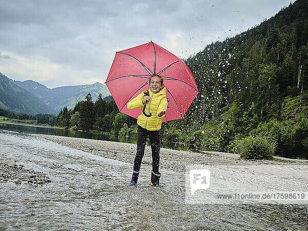 Happy girl with umbrella enjoying water splashing by lakeshore