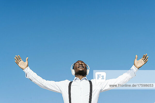 Man wearing headphones with hands outstretched on sunny day
