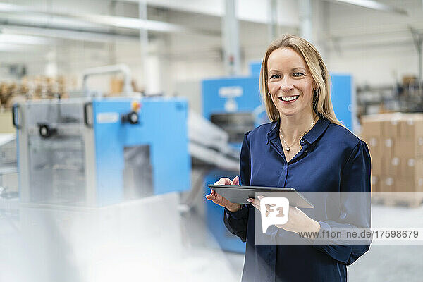 Happy businesswoman with tablet PC standing in factory